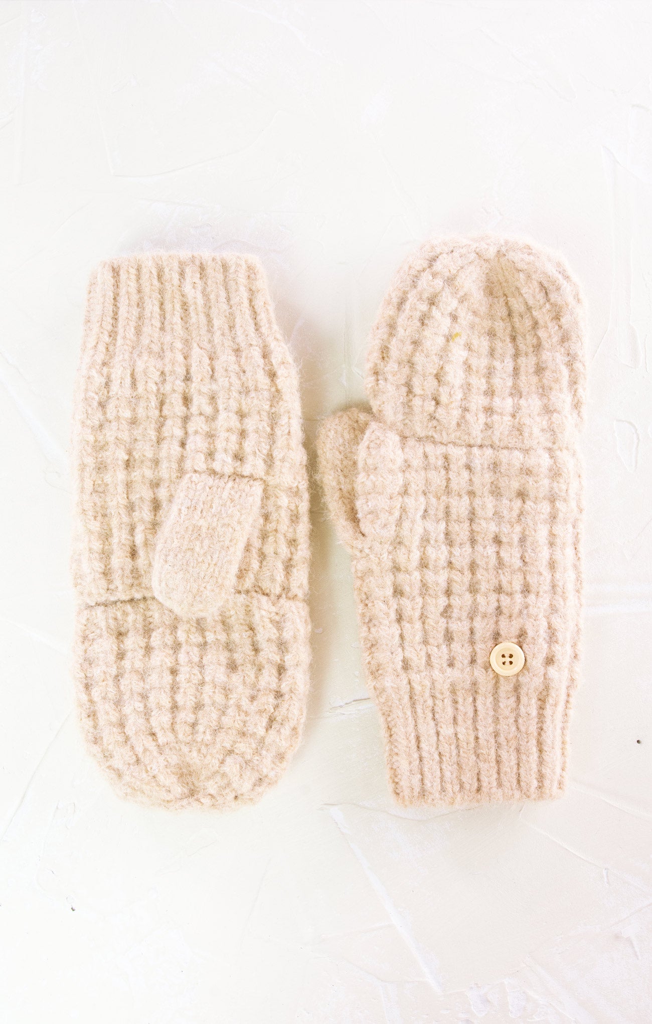 Pair of beige knitted mittens with a button on a white background