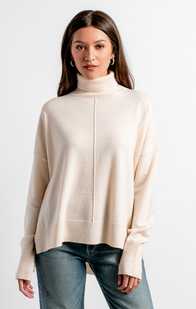 Woman wearing a beige turtleneck sweater and jeans on a white background