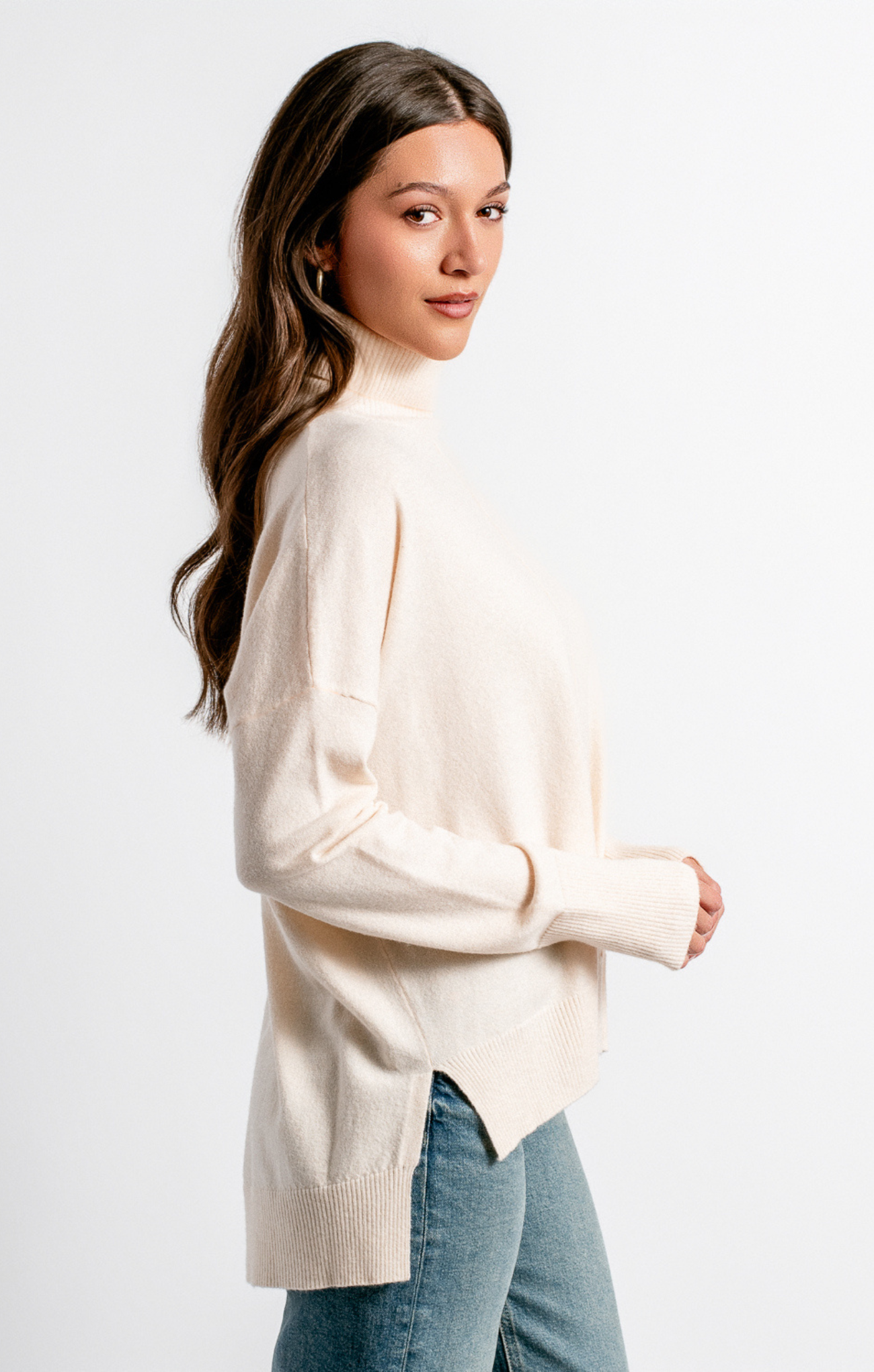 Woman wearing a beige sweater and blue jeans against a white background