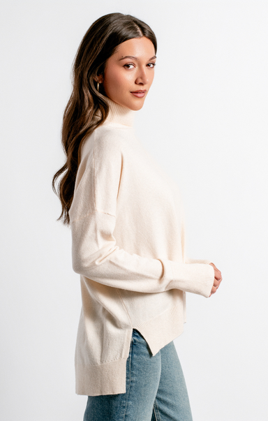 Woman wearing a beige sweater and blue jeans against a white background
