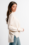 Woman wearing a beige sweater and blue jeans against a white background