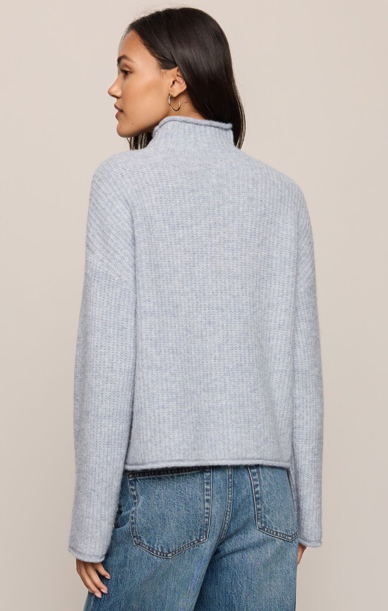 Woman wearing a light blue textured sweater and jeans on a beige background