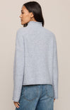 Woman wearing a light blue textured sweater and jeans on a beige background
