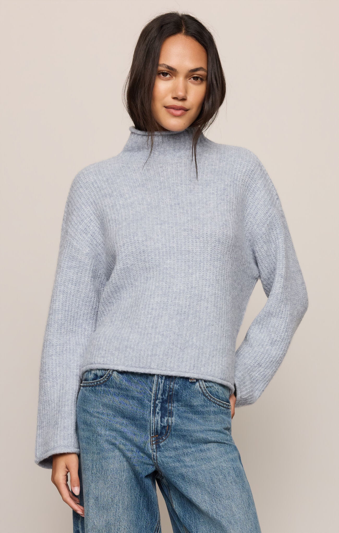 Woman wearing a light blue sweater and jeans against a beige background