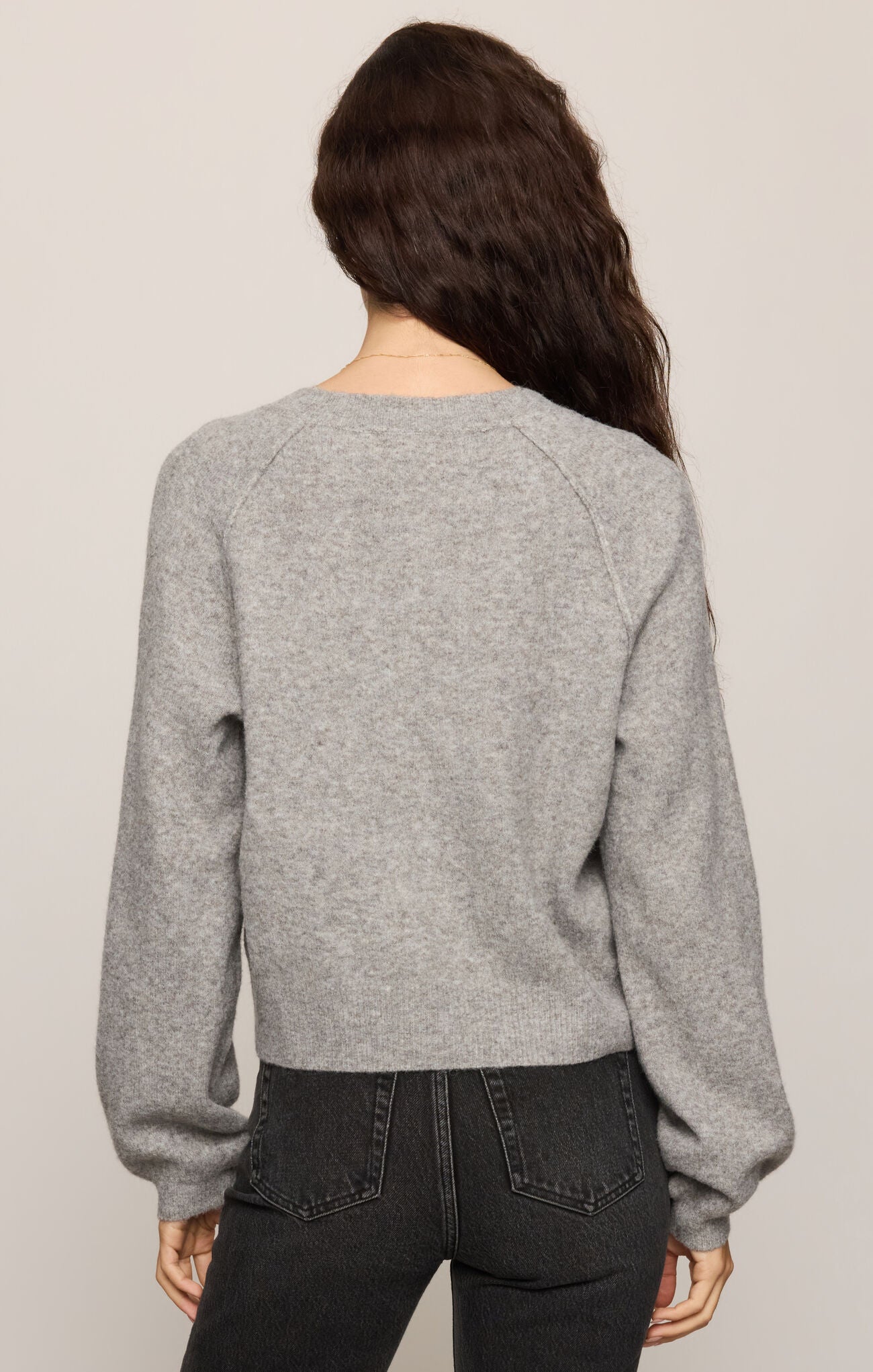 Person wearing a gray sweater and black pants on a plain background