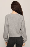 Person wearing a gray sweater and black pants on a plain background