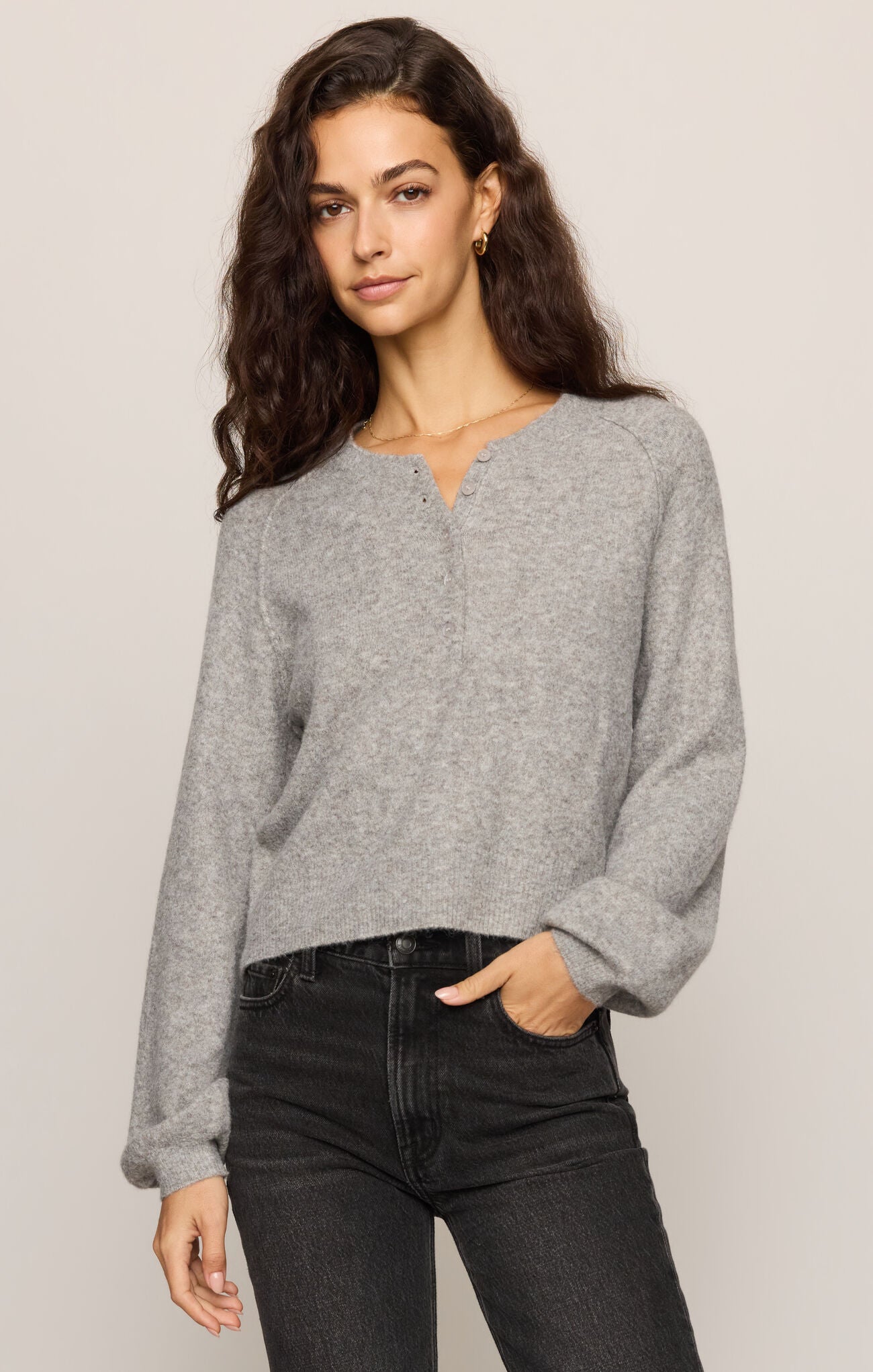 Woman wearing a gray sweater and black pants against a plain background