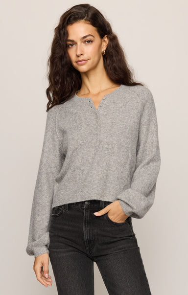 Woman wearing a gray sweater and black pants against a plain background