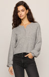 Woman wearing a gray sweater and black pants against a plain background