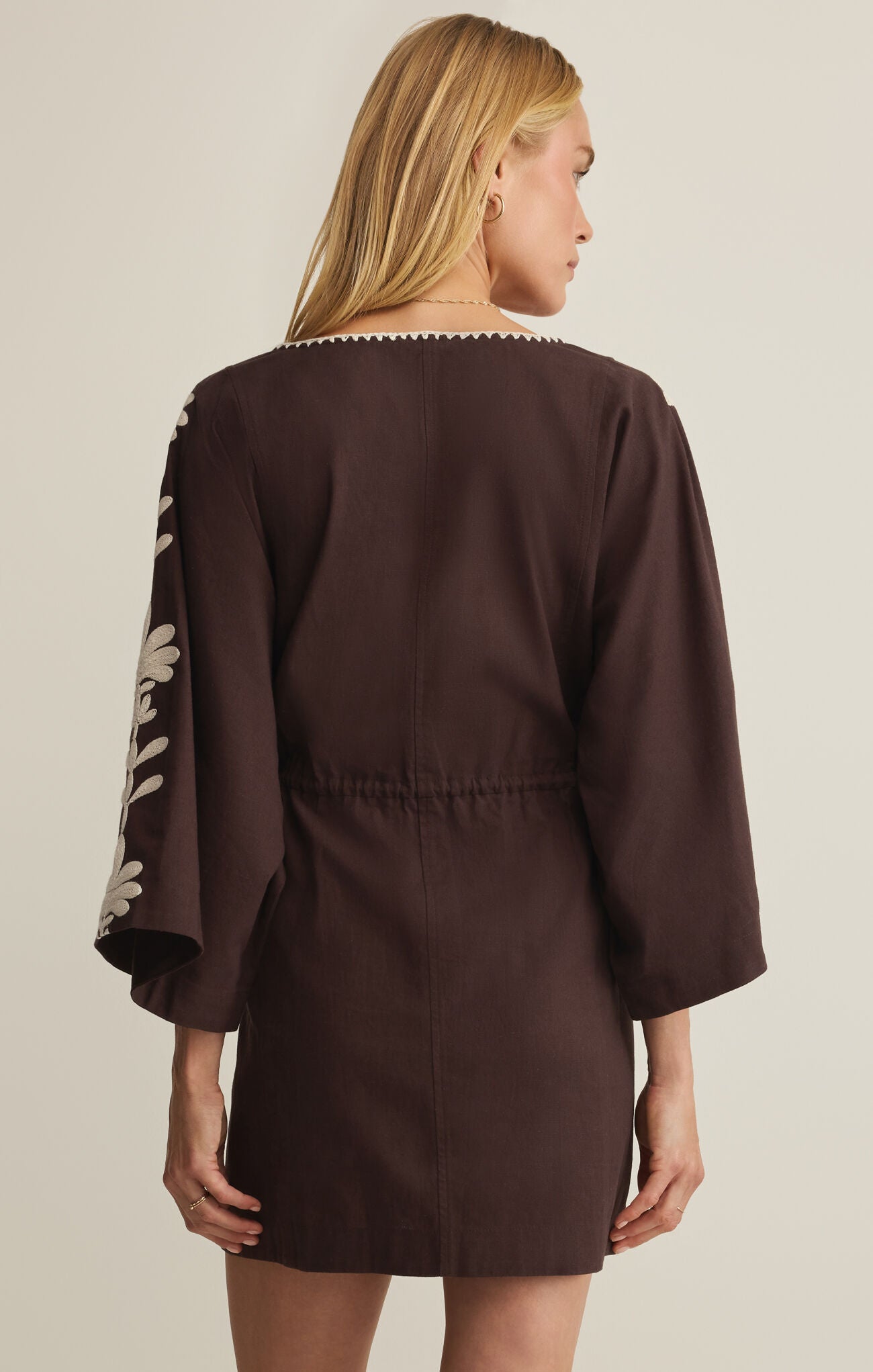 Woman wearing a brown dress with floral sleeves on a beige background