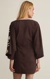 Woman wearing a brown dress with floral sleeves on a beige background