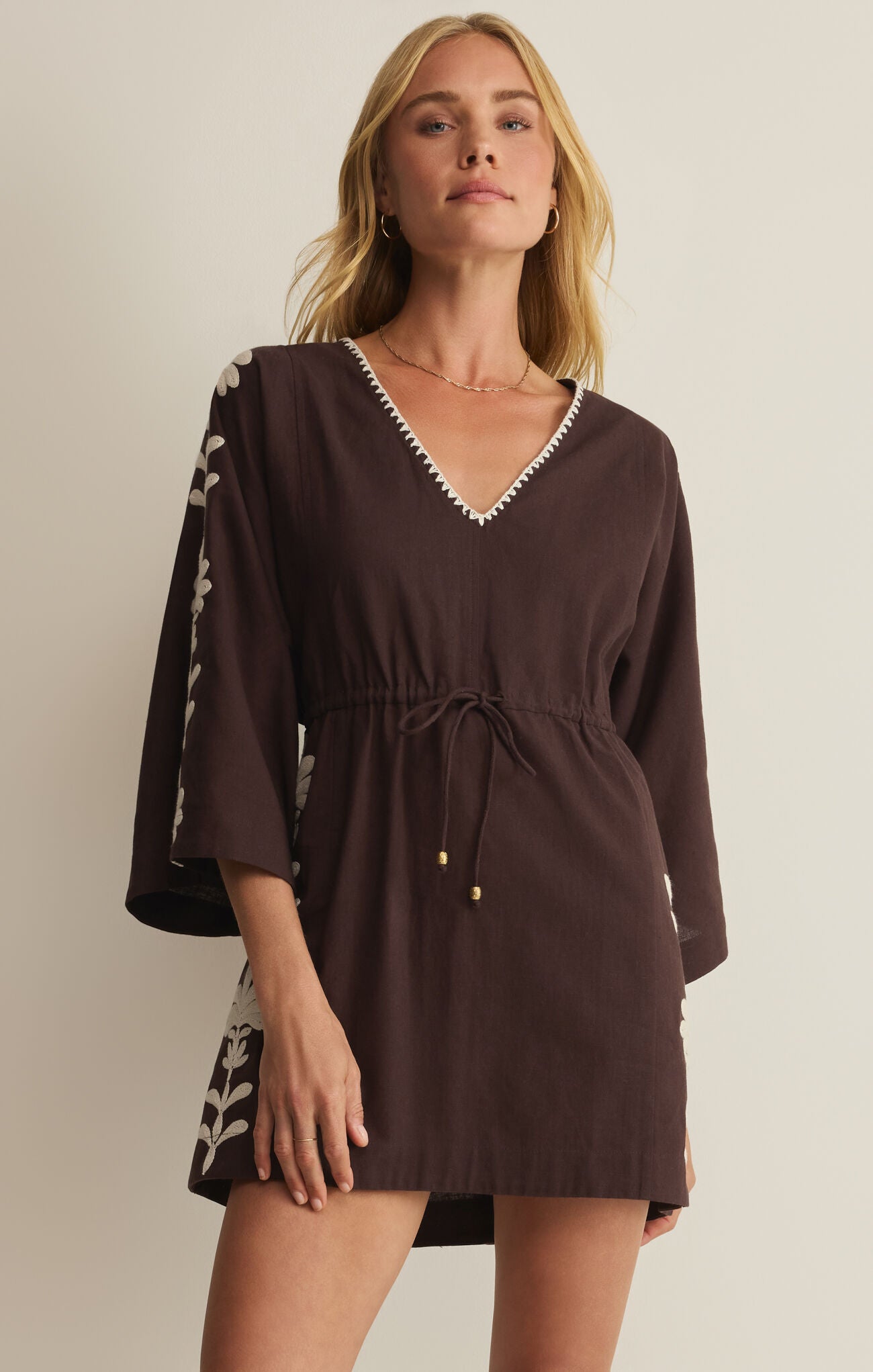 Woman wearing a brown dress with white trim against a plain background