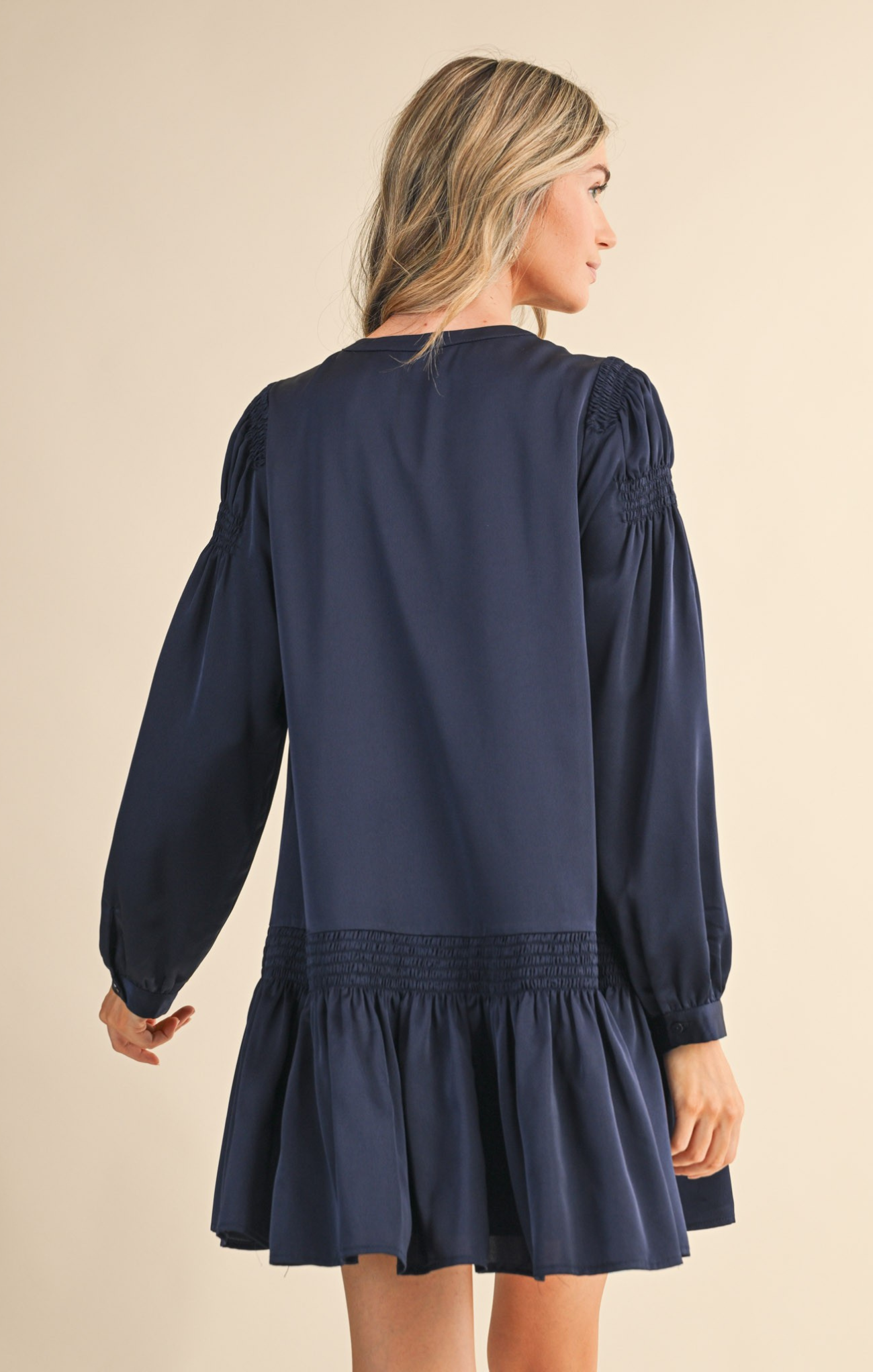 Navy blue dress with long sleeves and a ruffled skirt worn by a person on a beige background
