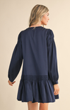 Navy blue dress with long sleeves and a ruffled skirt worn by a person on a beige background