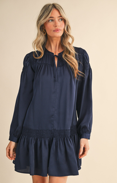 Woman wearing a navy blue dress with long sleeves on a beige background