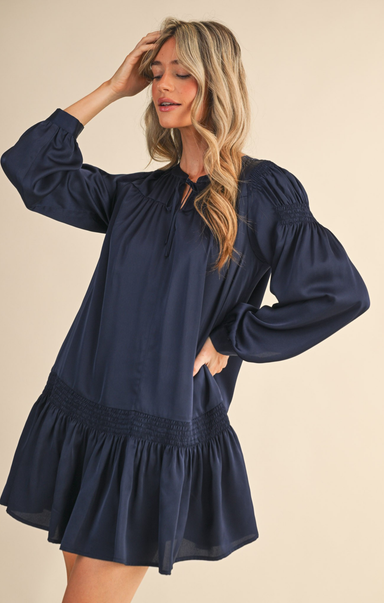 Woman wearing a navy blue dress with long sleeves on a beige background