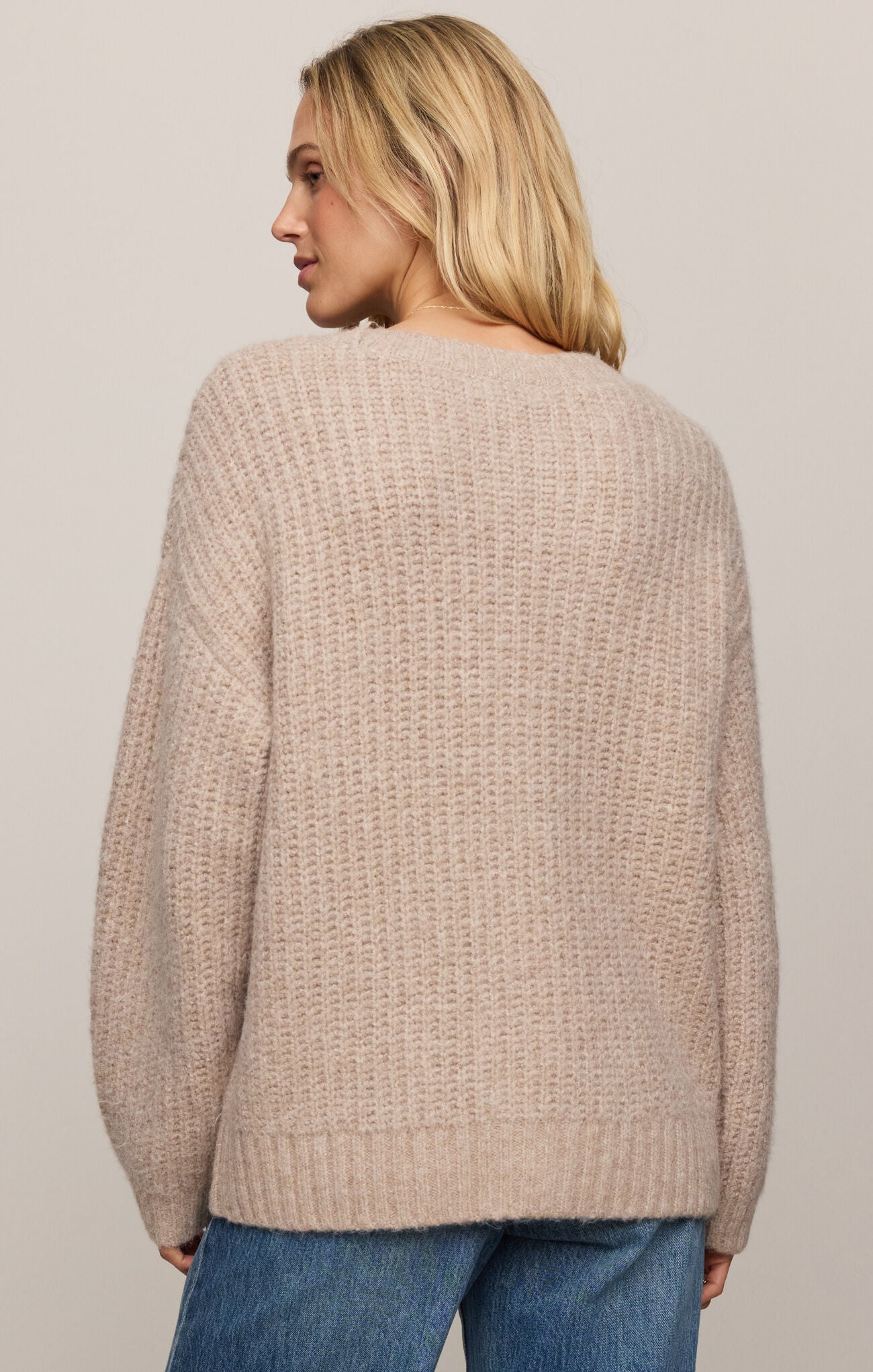 Woman wearing a beige knitted sweater and blue jeans on a plain background