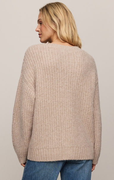 Woman wearing a beige knitted sweater and blue jeans on a plain background