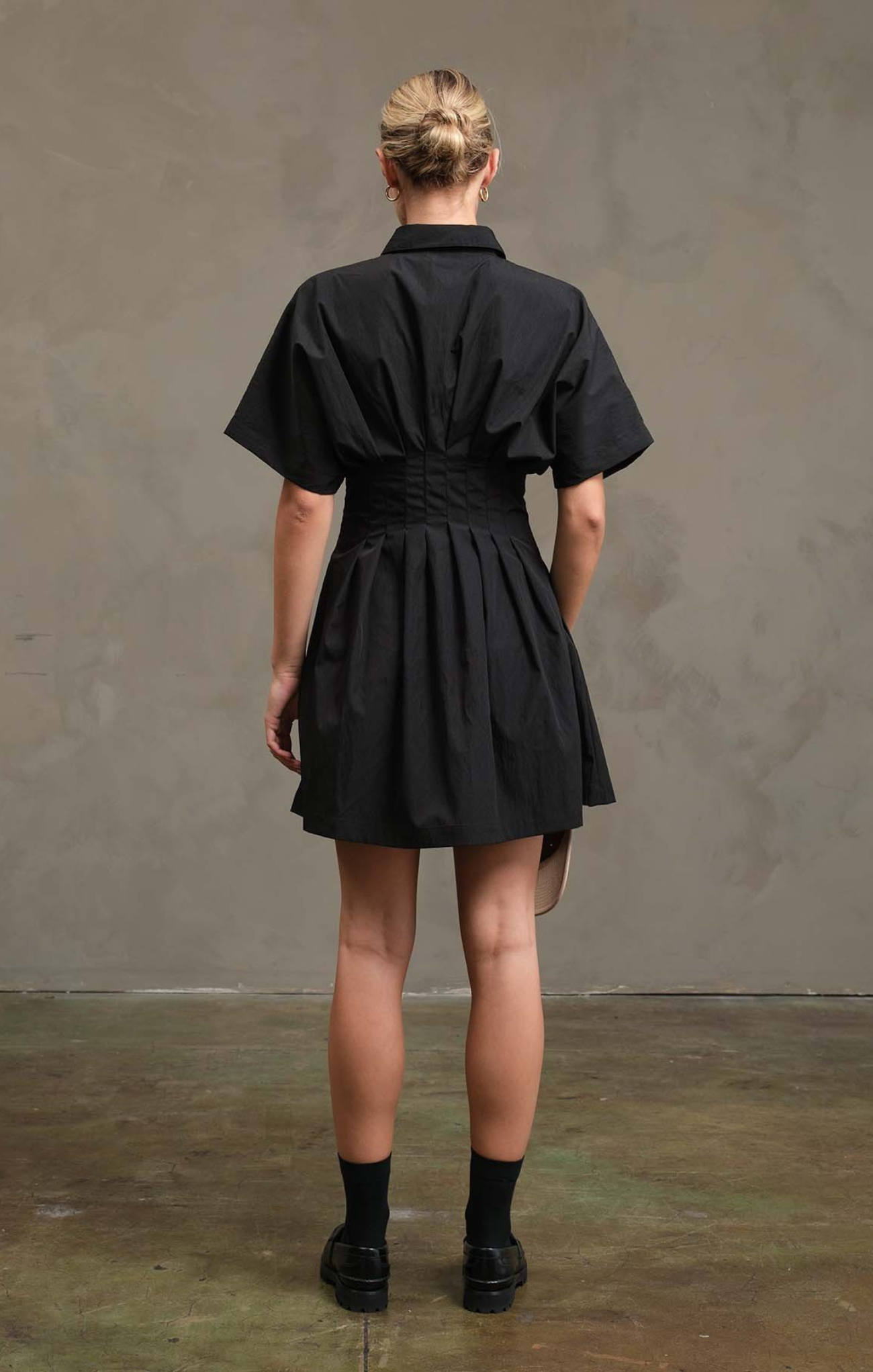 Person wearing a black dress against a gray wall.