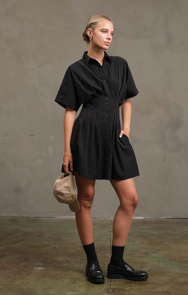 Woman wearing a black dress holding a beige bag against a plain background