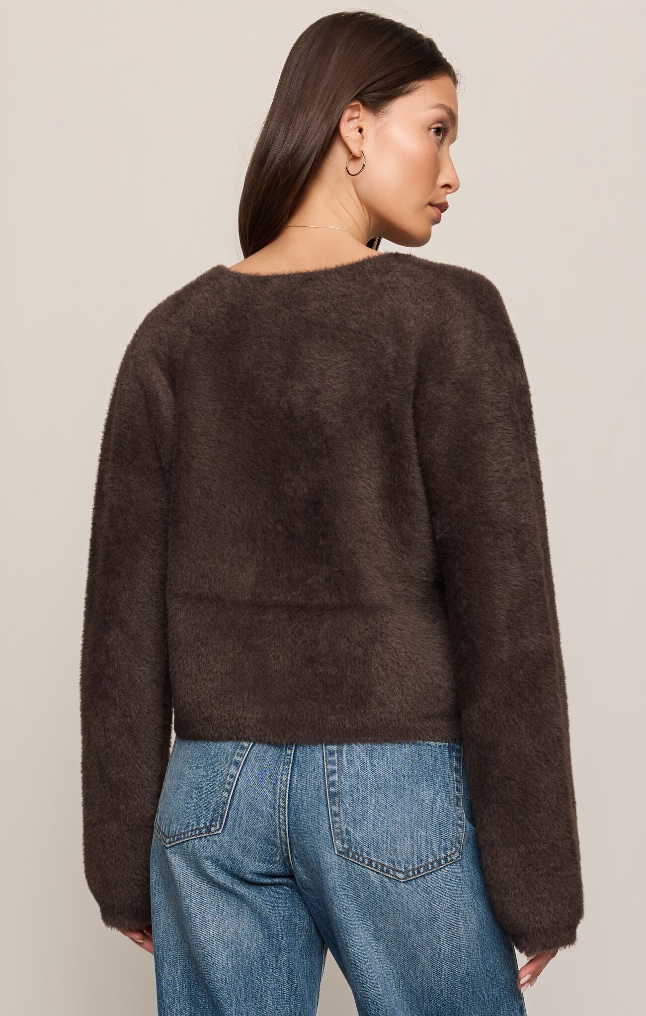 Woman wearing a brown sweater and blue jeans against a plain background