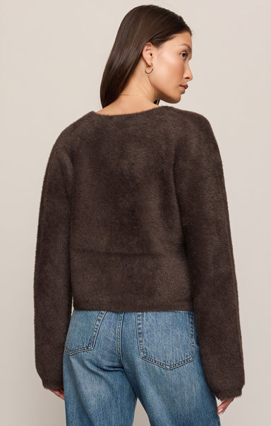Woman wearing a brown sweater and blue jeans against a plain background