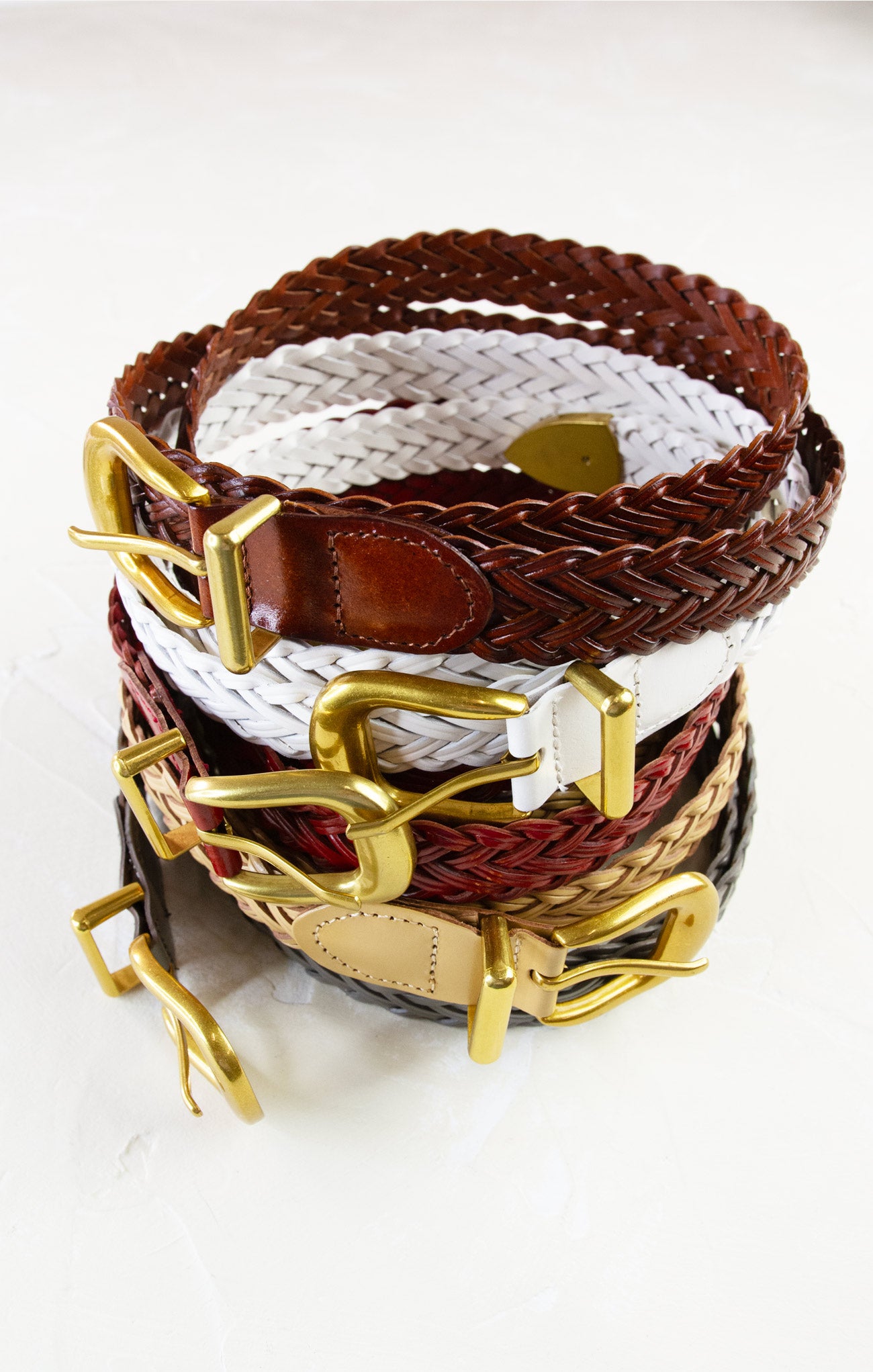 Stack of woven belts with gold buckles on a white background
