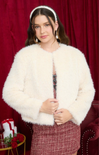 Woman wearing a white fur coat against a red curtain background