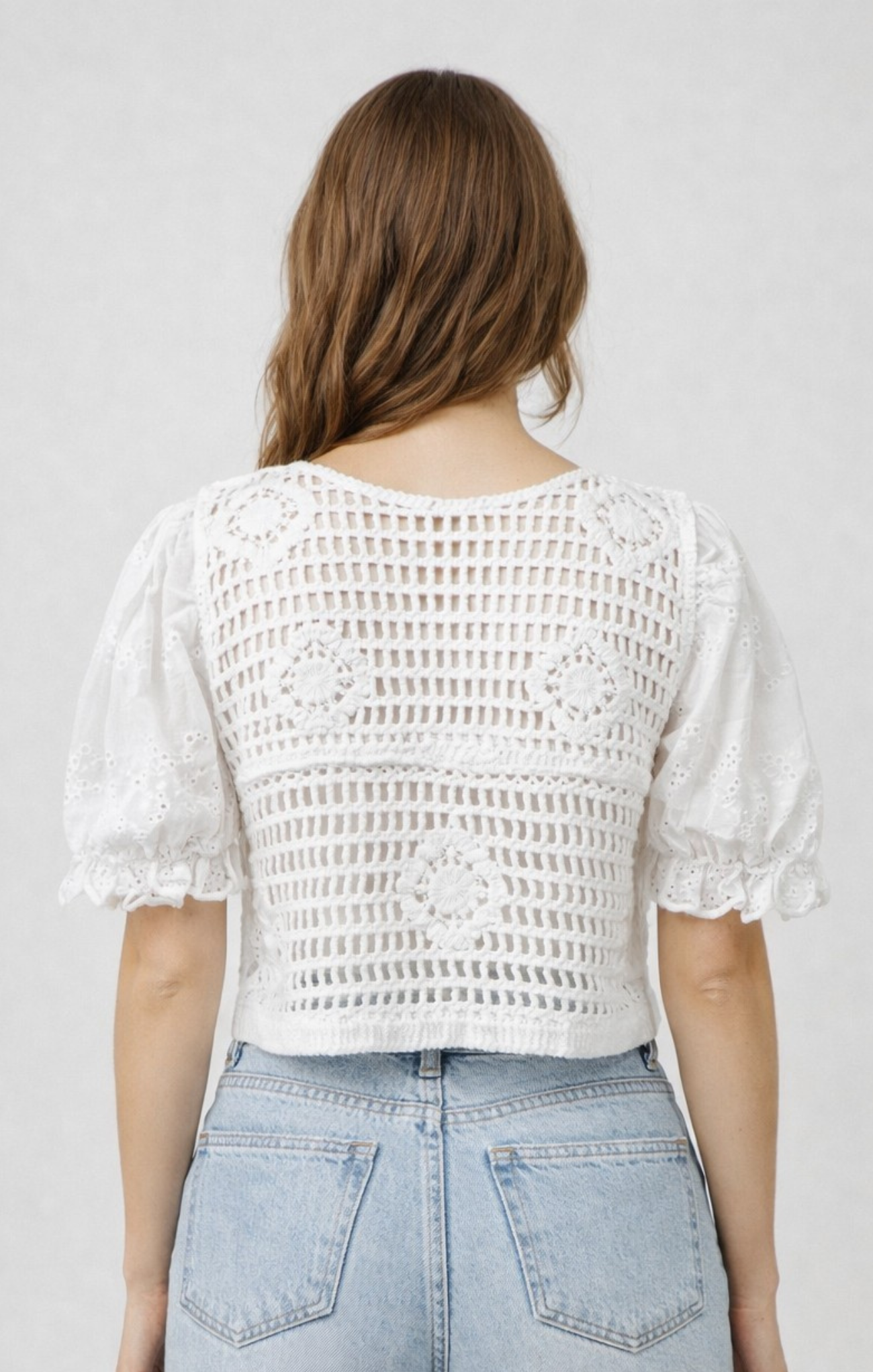 Person wearing a white crochet top and light blue jeans against a plain background