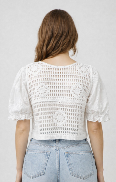 Person wearing a white crochet top and light blue jeans against a plain background