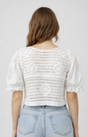 Person wearing a white crochet top and light blue jeans against a plain background