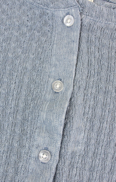 Close-up of a blue knitted cardigan with buttons on a textured fabric background