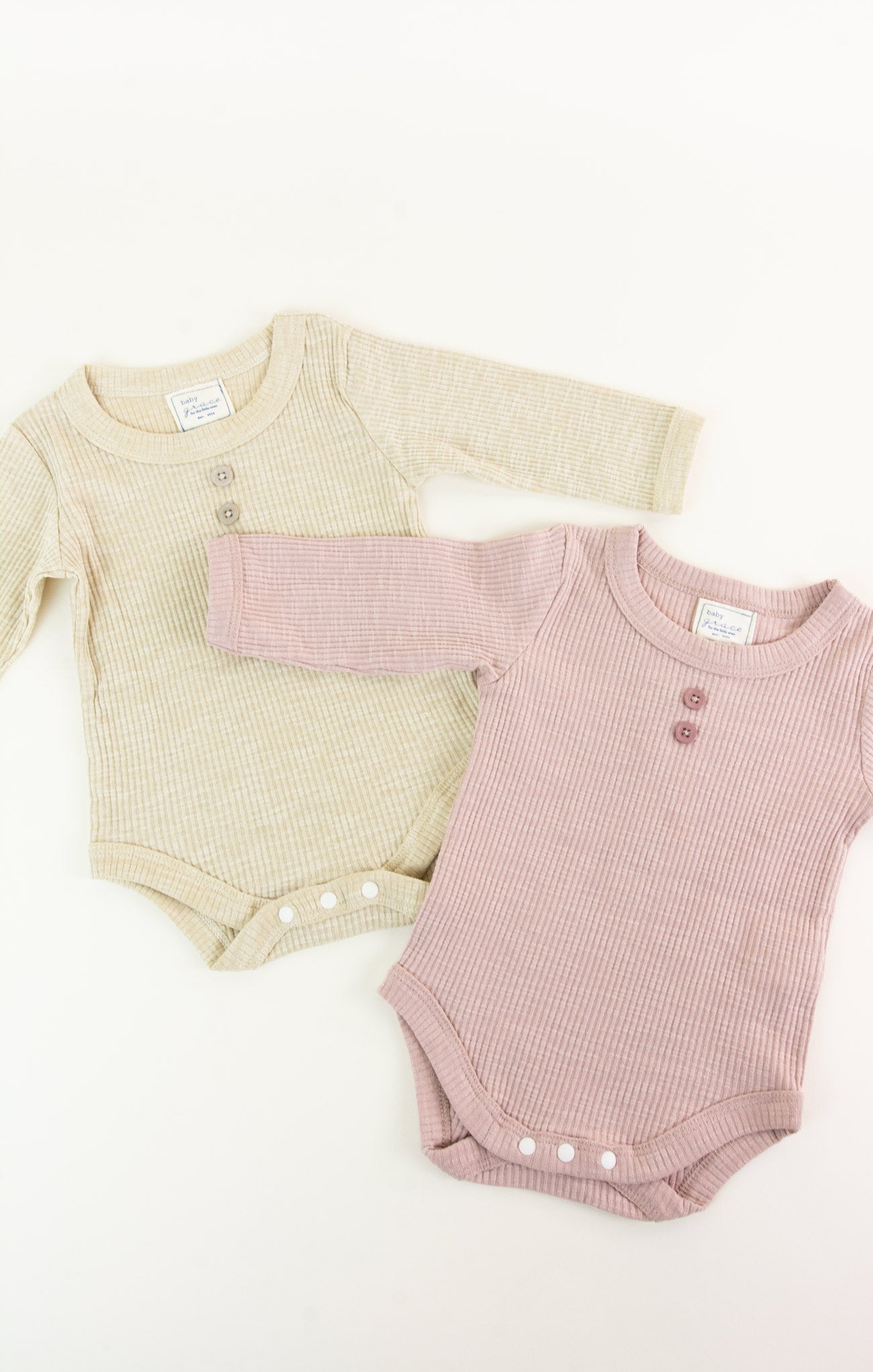 Two baby bodysuits, one beige and one pink, on a white background.