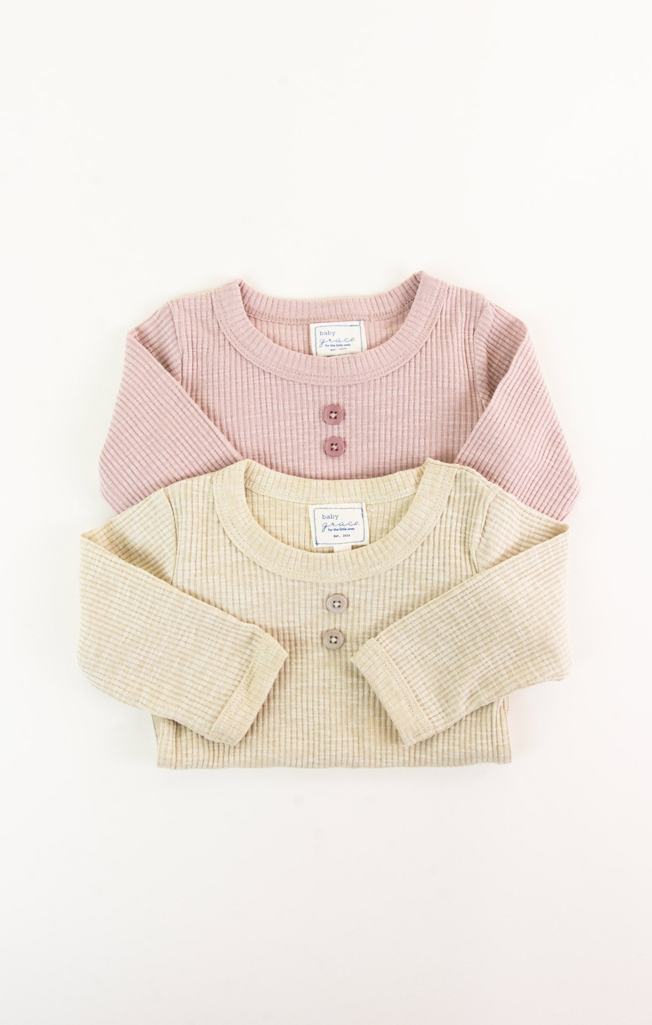 Two baby sweaters, one pink and one beige, on a white background