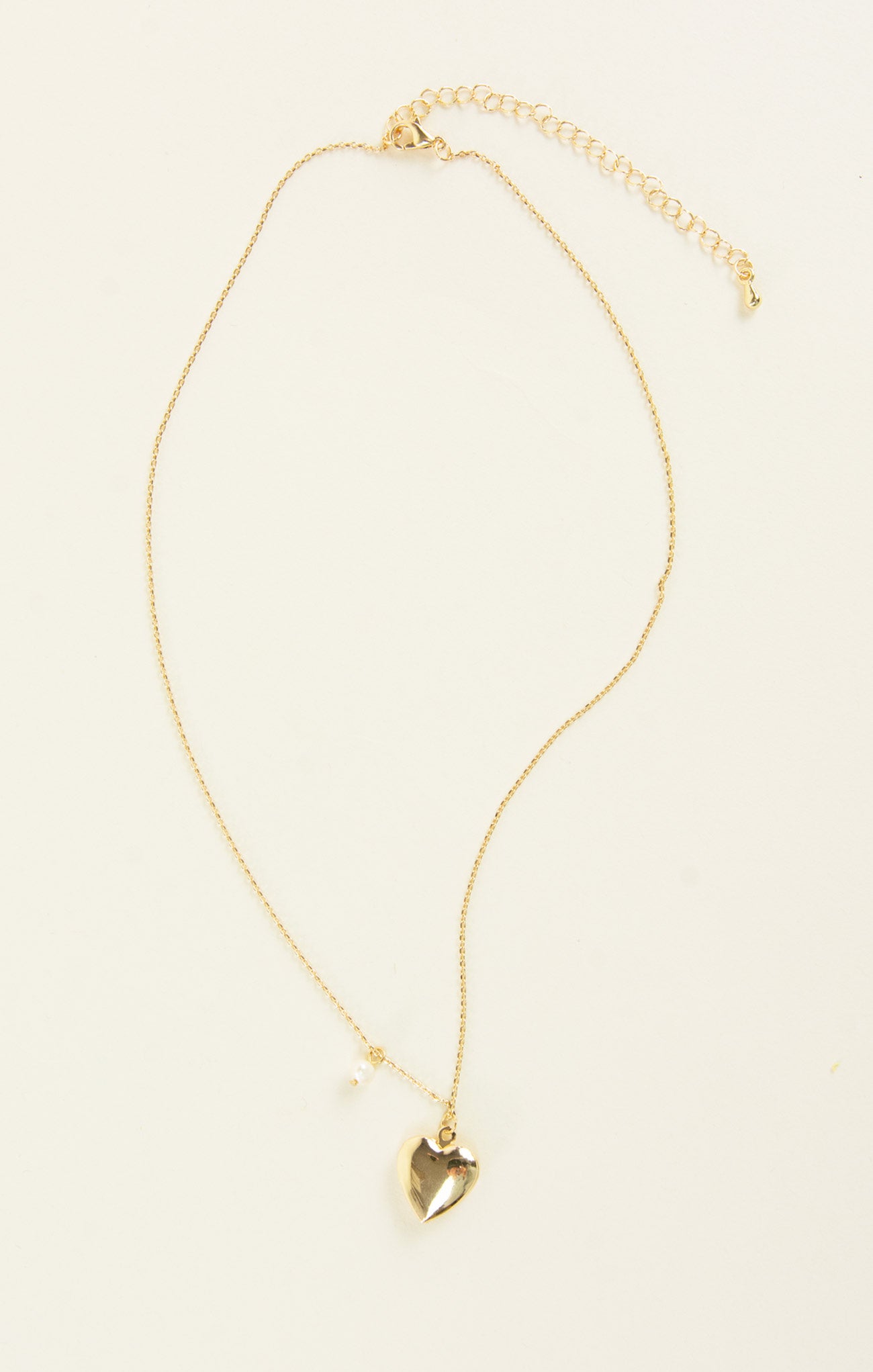 Gold necklace with a heart pendant on a beige background