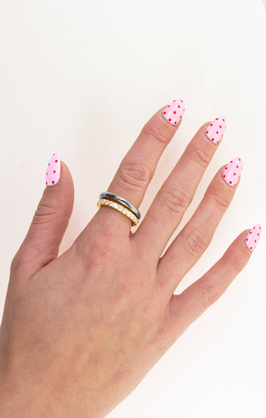 Hand with polka dot nail polish wearing two rings on a white background