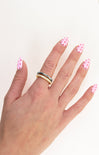 Hand with polka dot nail polish wearing two rings on a white background