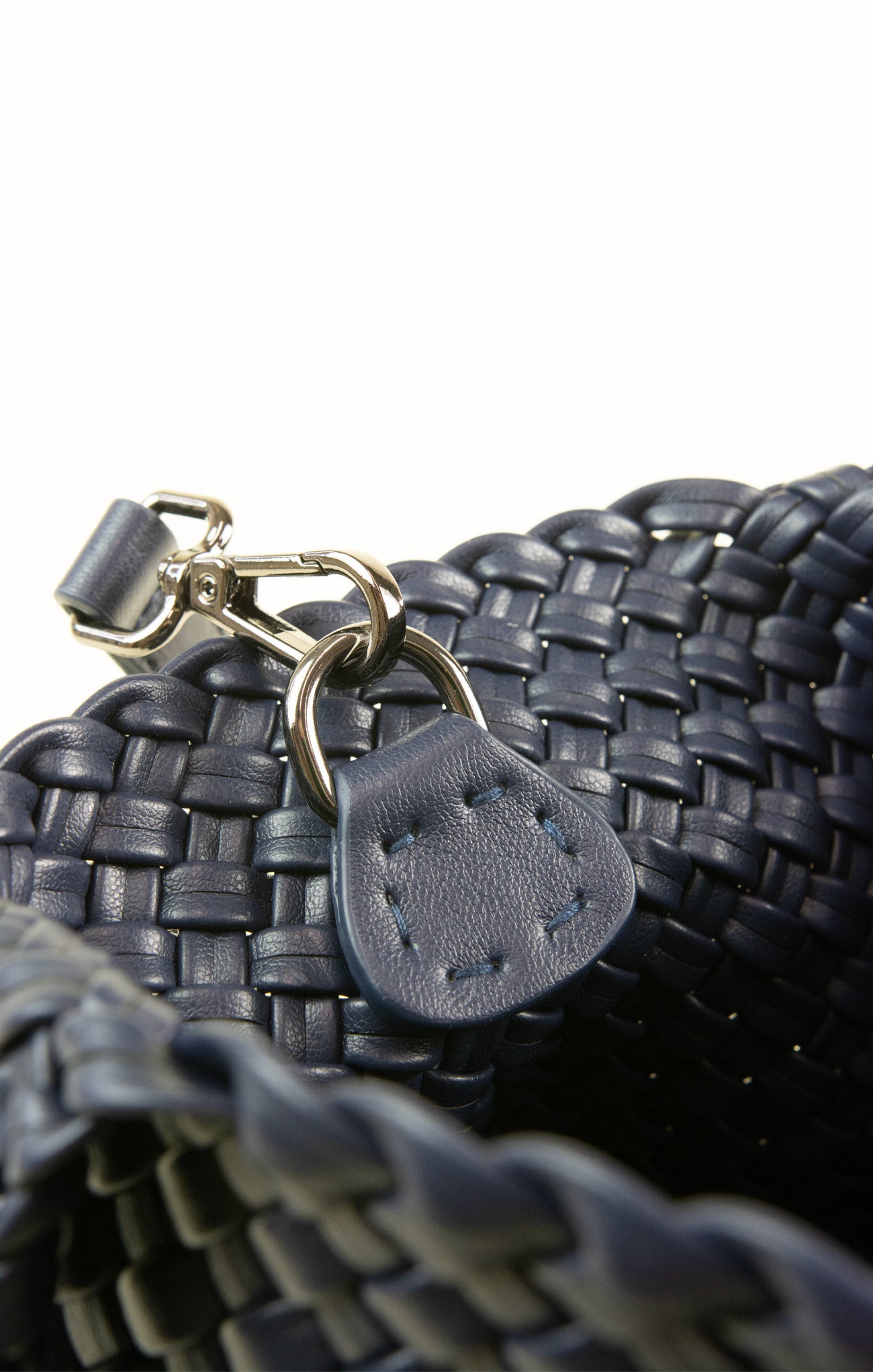 Close-up of a woven black handbag with a leather tag and clasp on a white background