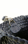 Close-up of a woven black handbag with a leather tag and clasp on a white background
