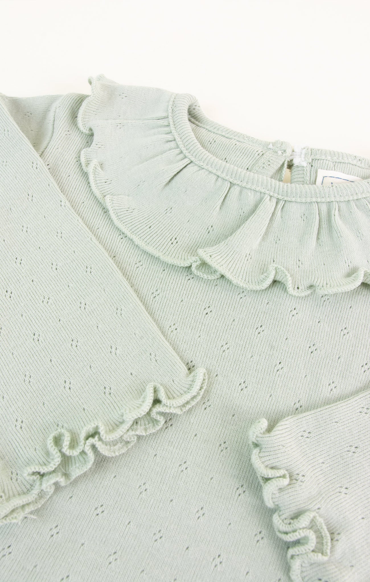 Light green baby outfit with ruffled details on a white background