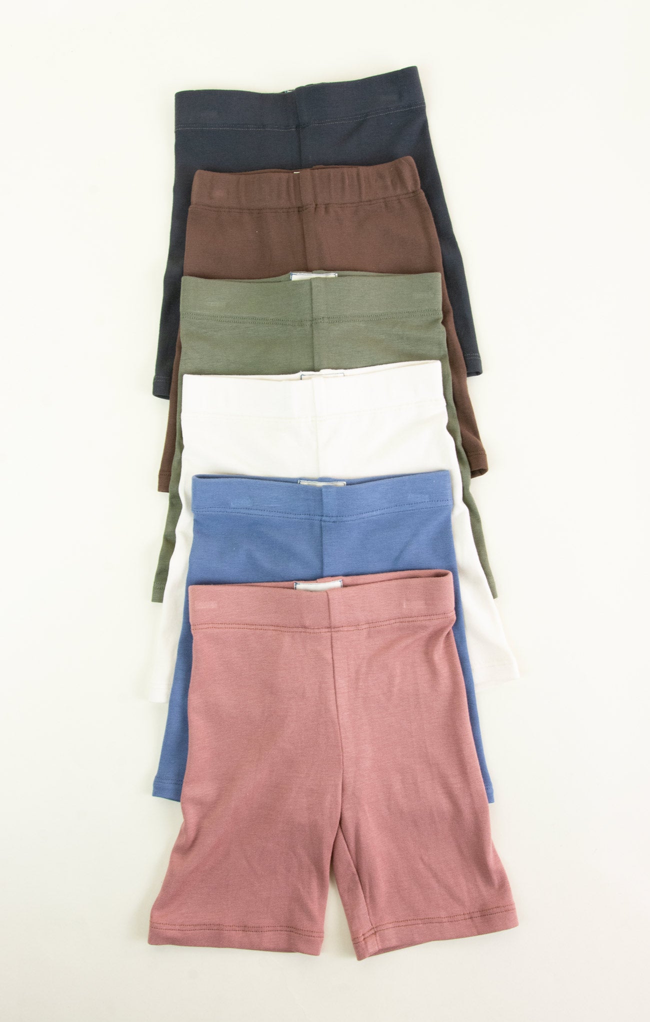Four pairs of shorts in different colors stacked on a white background