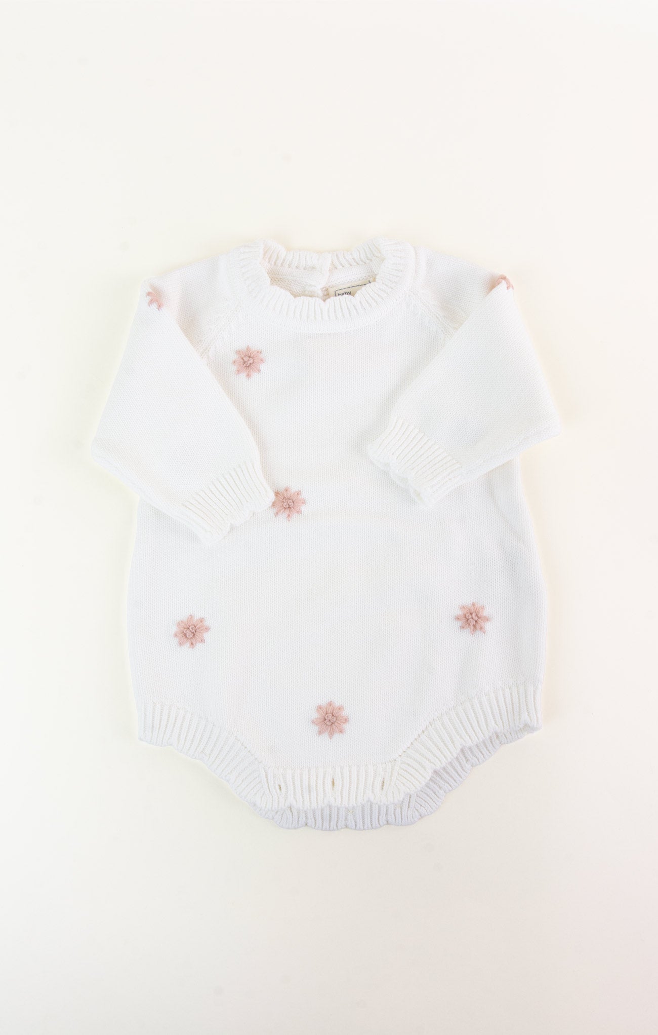 White baby romper with pink floral embroidery on a light beige background