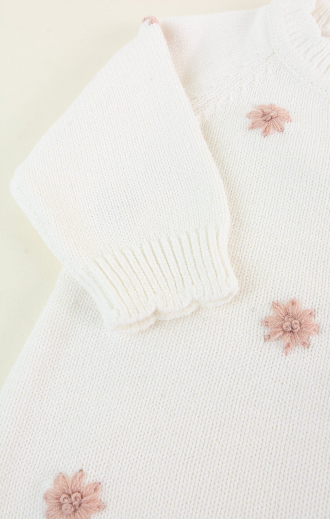 White knitted cardigan with pink floral embellishments on a light background
