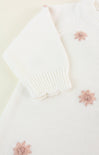 White knitted cardigan with pink floral embellishments on a light background