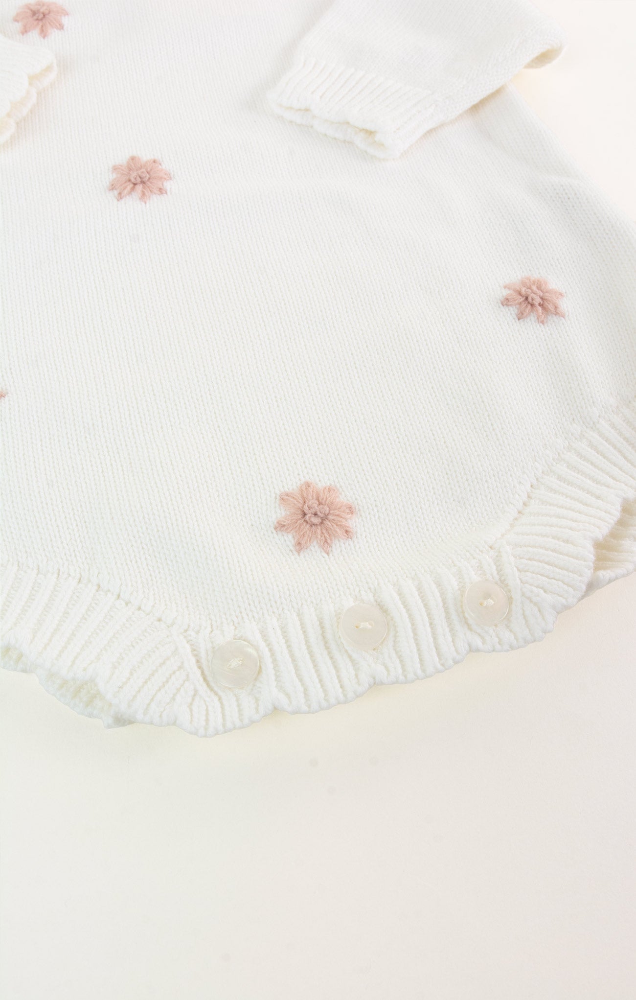 White knitted fabric with pink floral embellishments on a light pink background