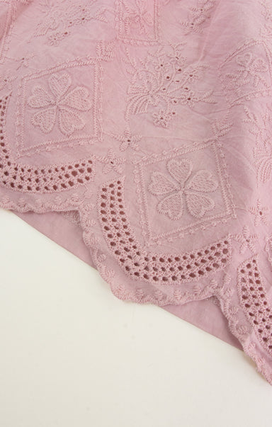Close-up of a pink embroidered fabric with intricate patterns on a white background