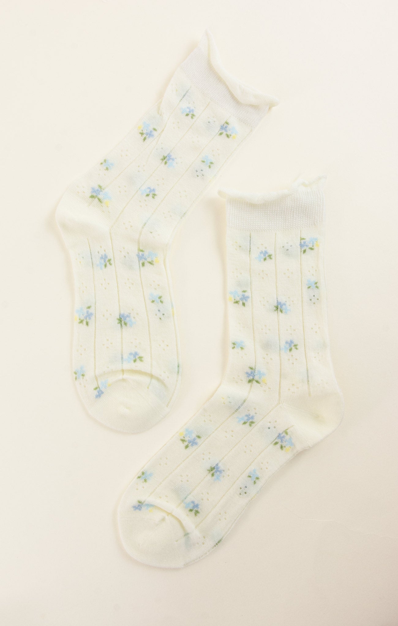 Pair of white socks with small blue floral patterns on a light beige background