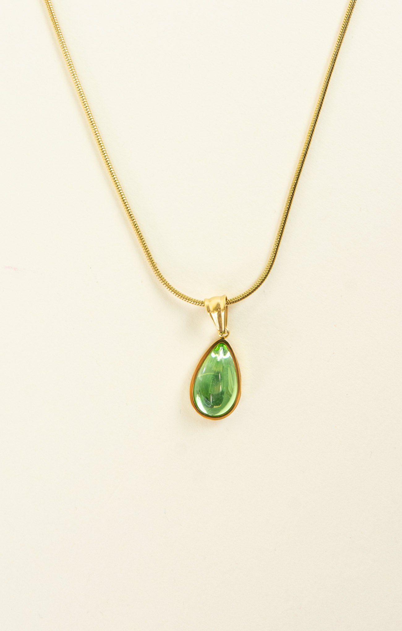 Gold necklace with a green teardrop pendant on a beige background