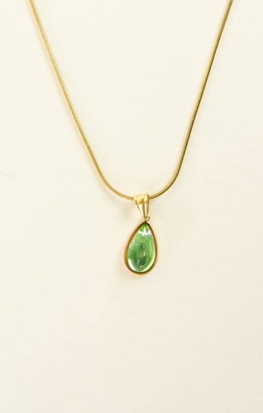 Gold necklace with a green teardrop pendant on a beige background