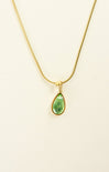 Gold necklace with a green teardrop pendant on a beige background